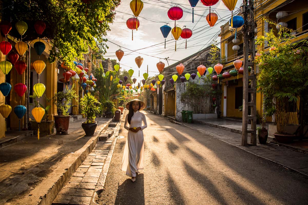 Vietnamese girl with white ao dai and non la in hoi an old town, walking on the lantern street